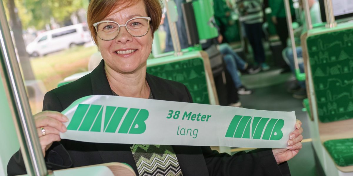 Birgit Münster-Rendel sitzt in der neuen Bahn. Sie hält ein Stück des Eröffnungsbandes in den Händen auf dem "38 Meter lang" steht.